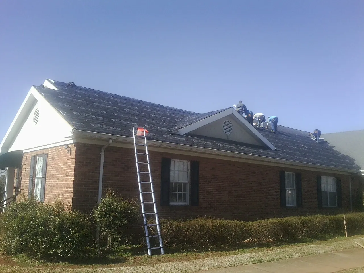 Crew tearing shingles off a brick ranch roof with a ladder set — Emergency Roof Repair work by our crew in Brandy Station