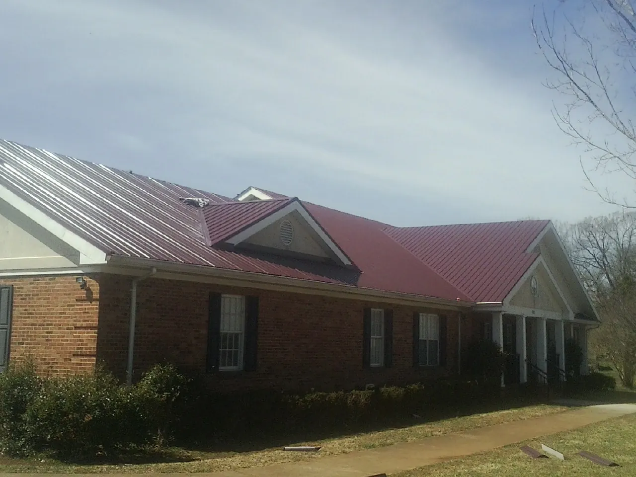 Red metal roof with gabled entries on a long brick building, from a Hail Damage Roof Repair job in Brandy Station