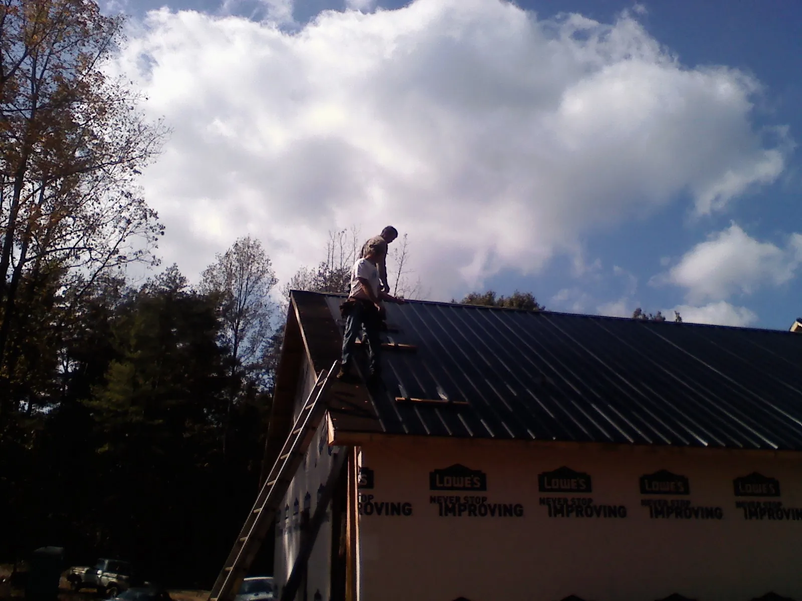 Roofer fastening dark metal panels high against a cloudy sky, from a Roof Inspection job in Brandy Station