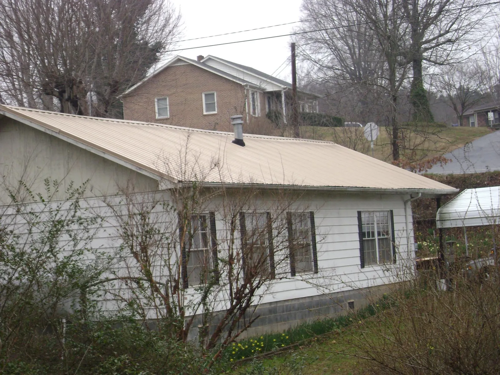 Tan metal roof on a white sided house set into a hillside — Commercial Roofing by Roofing Brothers in Brandy Station
